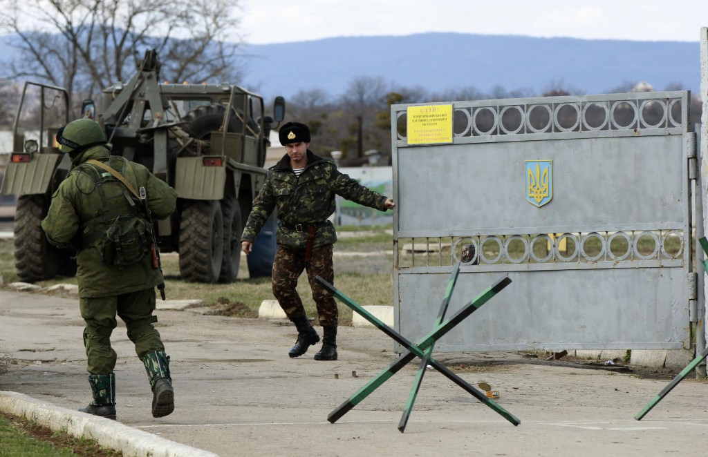 A Ukrainian serviceman closes a gate as an armed man, believed to be Russian serviceman, stands guard outside an Ukrainian military base in Perevalnoye